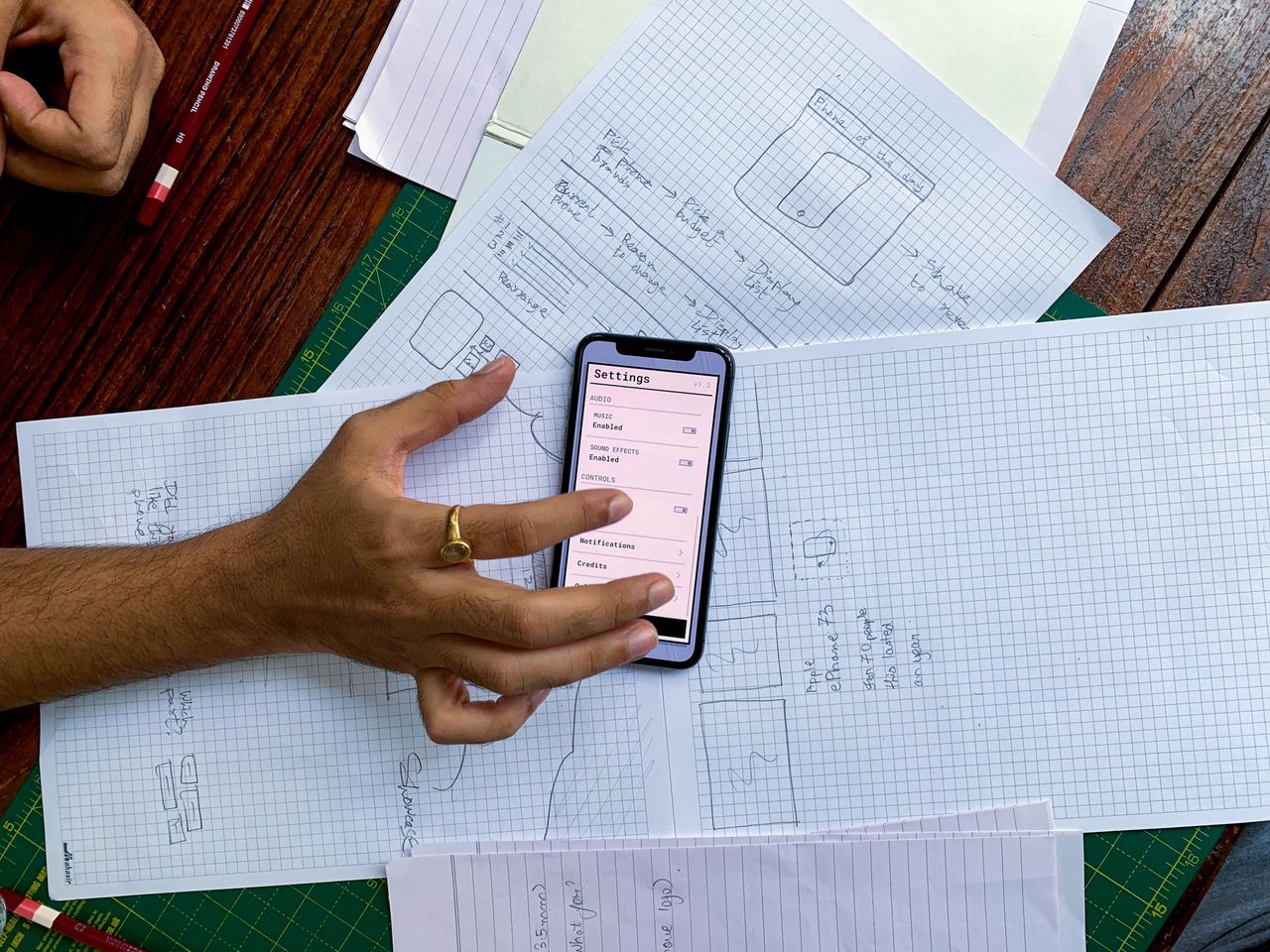 Hand holding smartphone over app design sketches on papers, top view.